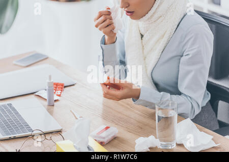 Ritagliato colpo di malati imprenditrice sciarpa in contenitore di contenimento di pillole al posto di lavoro Foto Stock