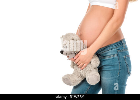 Vista ritagliata della donna incinta holding orsacchiotto vicino al suo ventre isolato su bianco Foto Stock