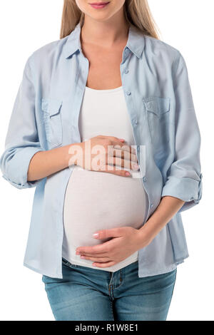 Ritagliato shot di sorridere donna incinta in jeans e maglietta tenendo la pancia con le mani isolato su bianco Foto Stock