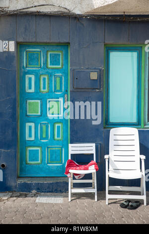 Due sedie vuote sul lungomare contro una parete blu e blu e verde, porta le sedie sono vuote, con un telo da spiaggia. Le persone sono andati a nuotare Foto Stock