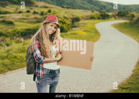 Bella giovane donna holding fustellato di cartone e autostop in strada del paese. Foto Stock