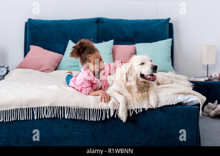 Adorable African American Bambino giacente sul letto e graffiare il retro di un cane Foto Stock