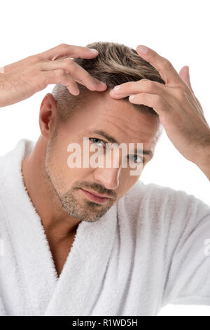 Ritratto di uomo adulto in accappatoio controllare se stesso per la perdita di capelli isolato su bianco Foto Stock