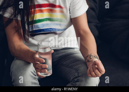 Ritagliato colpo di uomo in t-shirt con orgoglio bandiera tenendo un bicchiere di acqua e pillola Foto Stock