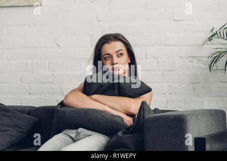 Riflessivo transgender giovane uomo seduto sul divano e guardando lontano da casa Foto Stock