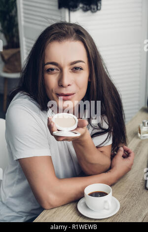 Close-up ritratto di Giovane sorridente transgender uomo soffiando trucco blush in telecamera Foto Stock