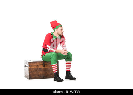 Malinconici uomo in elf natale costume seduto sulla cassa di legno isolato su bianco Foto Stock