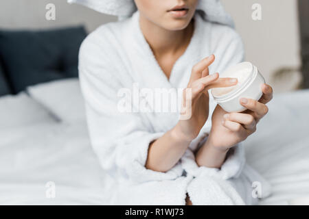 Vista ritagliata della donna con crema cosmetica in contenitore di plastica Foto Stock