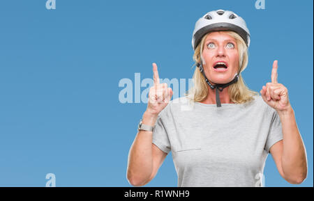 La mezza età caucasian ciclista donna che indossa il casco di sicurezza su sfondo isolato meravigliato e sorpreso cercando e dispositivo di puntamento con le dita e sollevato Foto Stock