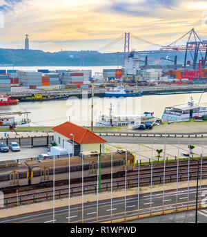 Il treno sulla Ferrovia dal porto commerciale con navi e contenitori, 25 de Abril ponte sul fiume Tago al tramonto, Lisbona, Portogallo Foto Stock