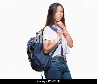 Giovane donna asiatica che indossa uno zaino e cuffie isolato su sfondo faccia seriamente pensando di domanda, molto confusa idea Foto Stock