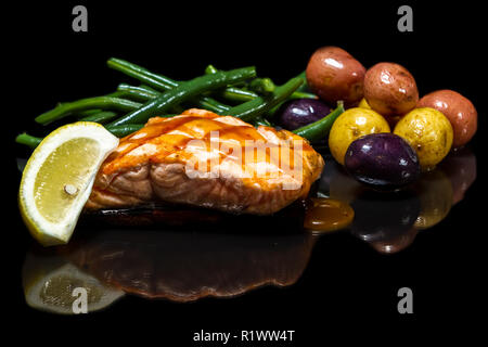 Delizioso salmone grigliato servito su un legno di cedro con il bambino le patate e i fagiolini verdi isolati su uno sfondo nero Foto Stock