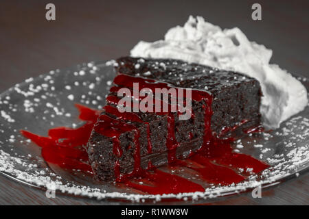 Fetta di una ricca e fitta torta al cioccolato senza farina servita con una salsa di lamponi Foto Stock