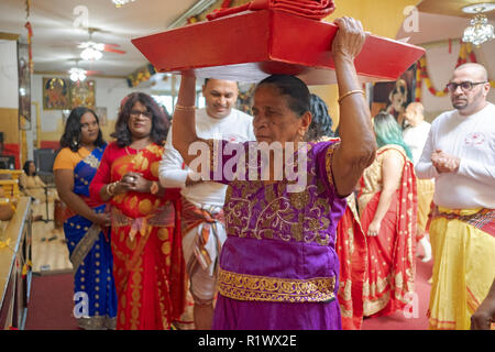 Circondato dalla sua famiglia, una vecchia donna Indù offerte porta alla divinità in un tempio in Ozone Park, Queens, a New York. Foto Stock