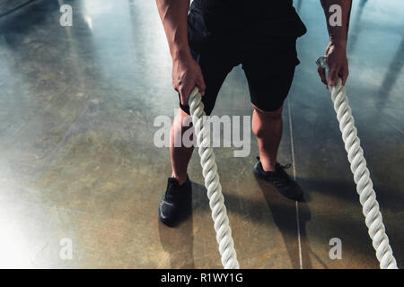 Vista ritagliata di uno sportivo che lavora fuori con funi di battaglia Foto Stock