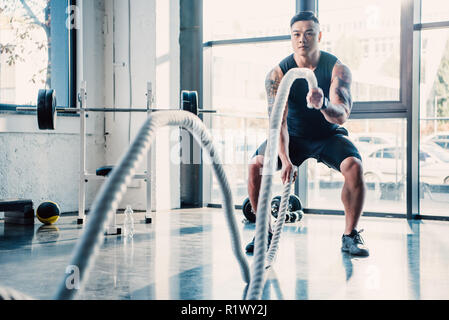 Giovane sportivo che lavora fuori combattimento con corde in palestra Foto Stock