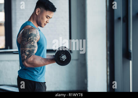 Concentrato vista laterale del giovane sportivo che esercitano con il manubrio in palestra Foto Stock