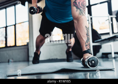Giovane atleta esercizio con manubri in palestra sul tappeto di sport Foto Stock
