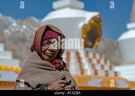Un ritratto di una vecchia donna locale, indossando occhiali, stupa buddisti e montagne coperte di neve in background Foto Stock