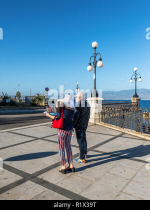 Reggio Calabria, Italia - 30 Ottobre 2017: coppia di viaggiatori usando la mappa per visite turistiche a waterfront promenade Lungomare Falcomata in Reggio Calabri Foto Stock