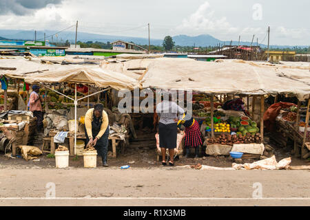 Una donna africana sta di fronte una esplorazione di stallo di frutta e verdura in vendita nel mercato, Kenya Foto Stock