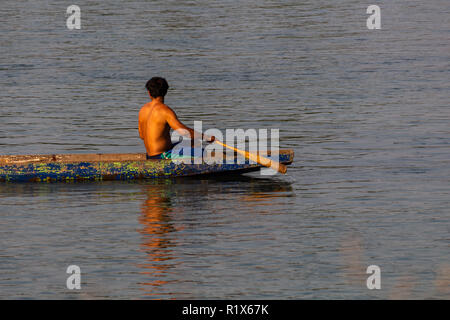 Don Det, Laos - Aprile 22, 2018: Locale uomo barca a remi in legno barca lunga oltre il fiume Mekong nel sud Laos Foto Stock