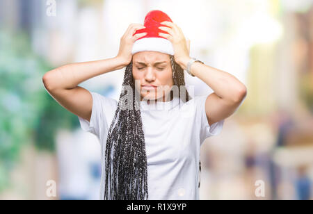 Giovani capelli intrecciati African American Girl con cappello a Natale su sfondo isolato che soffrono di mal di testa disperato e ha sottolineato perché il dolore di un Foto Stock