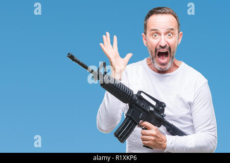 La mezza età senior annoso uomo delinquente tenendo la pistola arma su sfondo isolato molto felici ed eccitati, vincitore espressione celebrando la vittoria screami Foto Stock