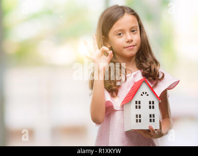 Bruna ragazza ispanica azienda piccola casa facendo segno ok con le dita, simbolo eccellente Foto Stock