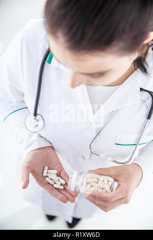 Medico donna su sfondo bianco pillole di fuoriuscite dal recipiente per la mano. Visualizzazione verticale Foto Stock