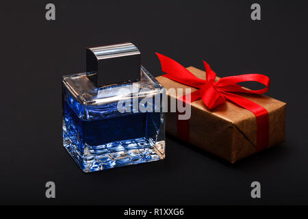 Confezione regalo legato con un nastro rosso e una bottiglia di profumo su sfondo nero. Giorno di celebrazione del concetto. Foto Stock