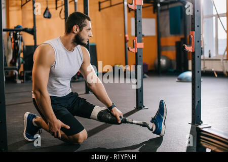 Bel giovane sportivo con gamba artificiale stretching vicino alla scaletta di ginnastica in palestra prima di allenamento Foto Stock