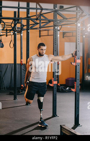 Bel giovane sportivo con gamba artificiale stretching vicino alla scaletta di ginnastica in palestra Foto Stock