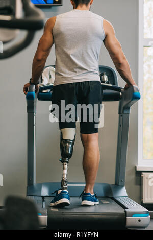 Vista posteriore del giovane sportivo con gamba artificiale camminando sul tapis roulant in palestra Foto Stock