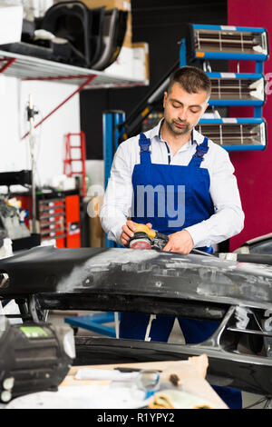 Professional repairman in auto officina sabbiatura paraurti di automobili, la preparazione per la verniciatura Foto Stock