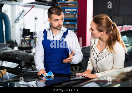 Auto gravi pittore discutendo con sorridente client femmina, di prelevare il colore della vernice in negozio di riparazioni auto Foto Stock