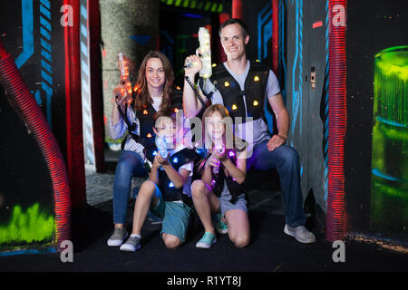 Ritratto di felici i bambini ed i loro genitori con le pistole laser durante il gioco lasertag in dark room Foto Stock