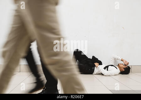 Giovane imprenditore asiatici sdraiato in passerella il pensiero del suo problema e guardare in modo premuto mentre la gente che passa da ( motion blur ) Foto Stock