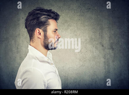 Vista laterale del moderno Adulto Uomo in camicia bianca cercando gravi su sfondo grigio Foto Stock
