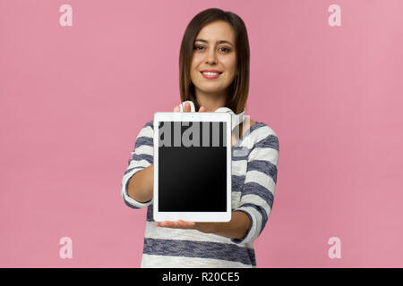 Happy brunette donna in eleganti maglione mostra vuoto tablet, isolato in rosa Foto Stock