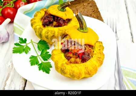 Due zucca gialla con ripieno di carne, i pomodori e i peperoni in un piatto, pane, aglio, prezzemolo e forcella su una tavola di legno Foto Stock