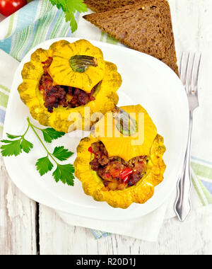 Due zucca gialla con ripieno di carne, i pomodori e i peperoni in un piatto, pane, aglio e prezzemolo con un tovagliolo su uno sfondo di tavole di legno sulla parte superiore Foto Stock