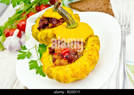 Due zucca gialla con ripieno di carne, i pomodori e i peperoni in un piatto, pane, aglio e prezzemolo con un tovagliolo sulla luce di sfondo di tavole di legno Foto Stock