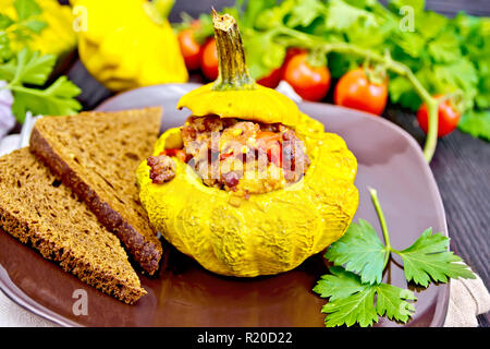 Squash giallo con ripieno di carne, pomodori e peperoni, pane nella piastra, i pomodori, il prezzemolo al buio su un pannello di legno Foto Stock