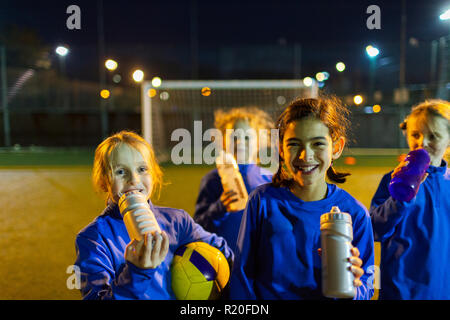 Ritratto di ragazze sorridenti soccer team prendendo una pausa dalla pratica, acqua potabile sul campo di notte Foto Stock