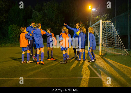 Ragazze Calcio team ascolto di coach sul campo di notte Foto Stock