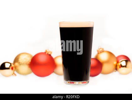 Completa di vetro pinta di birra scura o stout ale con sfocate baubles di natale in background su bianco Foto Stock