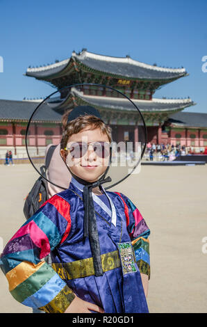 Un ragazzo sorrisi e pone per un ritratto indossando il tradizionale abito coreano di fronte a un cancello in Gyeongbokgung Palace a Seul, in Corea del Sud. Foto Stock