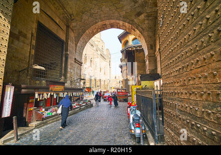 Il Cairo, Egitto - 21 dicembre 2017: l'auto e pedoni utilizzare stretto passaggio storico attraverso il Bab Zuwayla gate con piccoli negozi di mercato all interno di essa Foto Stock