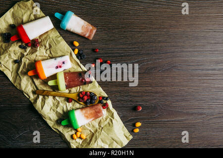 Appartamento vista laici del sacco di casa fatta frigo frullato congelati succhi yogurt gelato con frutti di bosco sul buio drammatico sfondo di legno. Snack sani c Foto Stock